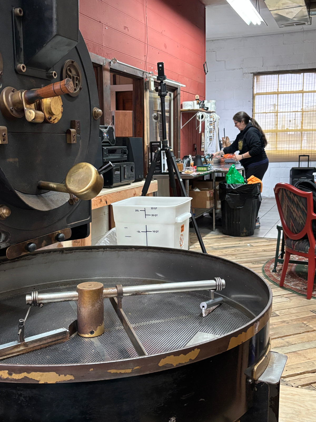 The roaster in motion — drum, beans cooling, hands at the tray.